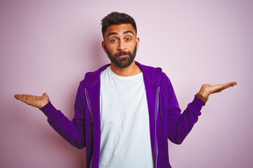 Young indian man wearing purple sweatshirt standing over isolated pink background smiling showing...