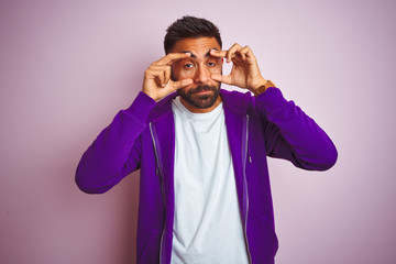 Young indian man wearing purple sweatshirt standing over isolated pink background Trying to open eyes with fingers, sleepy and tired for morning fatigue