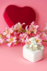 ceramic white casket with a teddy bear on a background of pink flowers and hearts
