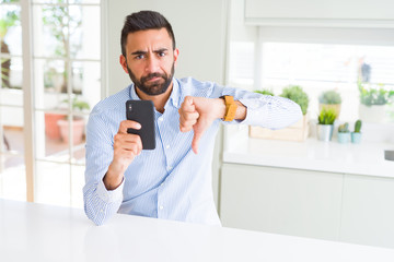 Handsome hispanic business man using smartphone with angry face, negative sign showing dislike with thumbs down, rejection concept