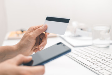 In hand is a blank white credit card mockup and mobile phone for internet payment.  