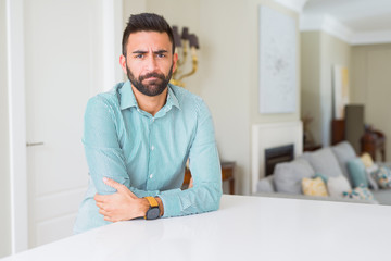 Handsome hispanic man at home skeptic and nervous, disapproving expression on face with crossed...