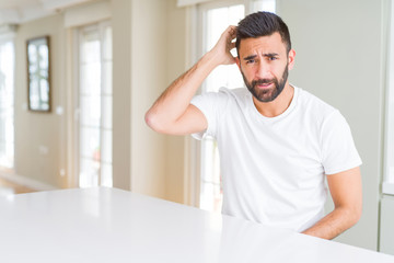 Handsome hispanic man casual white t-shirt at home confuse and wonder about question. Uncertain with doubt, thinking with hand on head. Pensive concept.