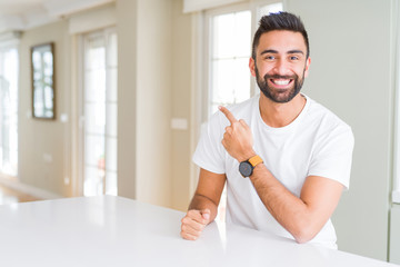 Handsome hispanic man casual white t-shirt at home cheerful with a smile of face pointing with hand and finger up to the side with happy and natural expression on face