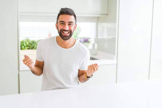 Handsome hispanic man casual white t-shirt at home celebrating surprised and amazed for success with arms raised and open eyes. Winner concept.