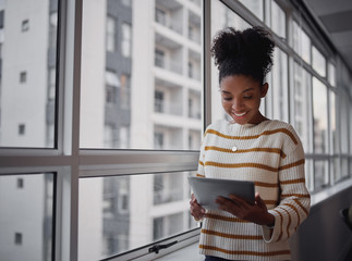 Attractive businesswoman using a digital tablet while standing in front of windows in an office...