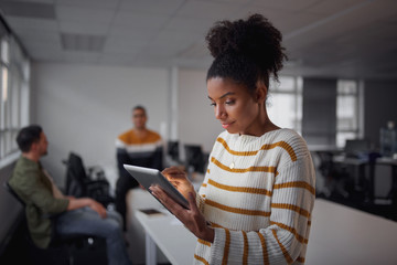 Portrait of a young Brazilian businesswoman using tablet and her colleagues working together in the background in South America