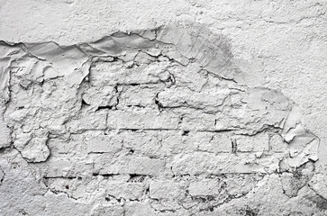 Part of a white wall with crumbling plaster, from under which bricks are visible. Background, texture.