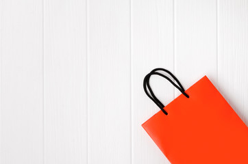 Orange paper shopping bag with black handles on the white wooden background