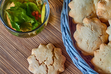 Biscuits in the wicker basket from newspaper tubules and a transparent cup of green tea with mint and red currants on brown wooden background. Closeup, selective focus