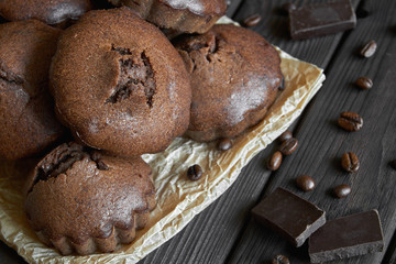 A group of homemade chocolate muffins on parchment with coffee beans and pieces of chocolate. Dark wooden background, closeup, selective focus