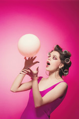 Cheeky girl with pink balloon on pink background in body, with curlers on head. Pretty sexy woman with sweet makeup attractively posing in studio