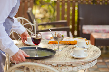 the waiter puts a glass of red wine on the table in a outdoor cafe.