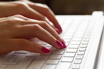Hands of a girl typing on a white laptop keyboard. Closeup