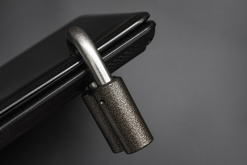 Locked steel padlock in a drilled hole of the black laptop on dark background. Concept of protecting personal data on a computer. A laptop is locked with a lock. Closeup, selective focus