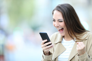Excited woman finds good offers on phone in the street