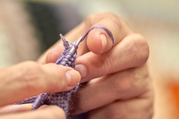 Woman is knitting a blue warm sweater. A hobby of elderly woman is knitting. Closeup view of knitting loop. Selective focus