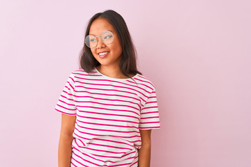 Fototapeta premium Young chinese woman wearing striped t-shirt and glasses over isolated pink background looking away to side with smile on face, natural expression. Laughing confident.