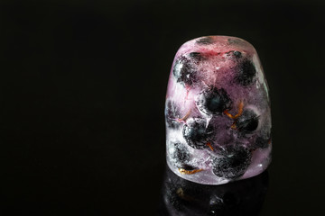 Black currant berries frozen in ice with reflection on dark background. Closeup, selective focus