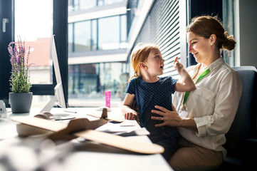 A businesswoman with small daughter sitting in an office, working.