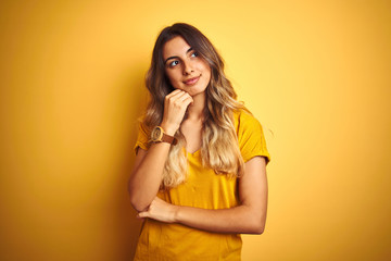 Young beautiful woman wearing t-shirt over yellow isolated background with hand on chin thinking about question, pensive expression. Smiling with thoughtful face. Doubt concept.