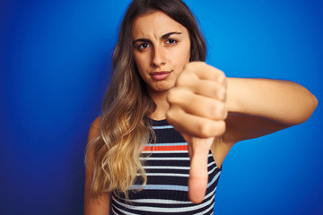Young beautiful woman wearing stripes t-shirt over blue isolated background with angry face,...