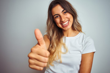 Young beautiful woman wearing t-shirt over white isolated background happy with big smile doing ok sign, thumb up with fingers, excellent sign