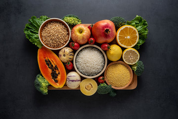 a pot of fresh seasonal fruits and vegetables and grains of legumes on a black background