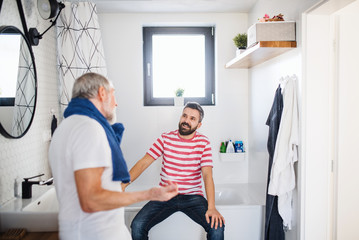 An adult hipster son and senior father in bathroom indoors at home, talking.