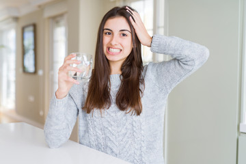 Beautiful young woman drinking a fresh glass of water stressed with hand on head, shocked with shame and surprise face, angry and frustrated. Fear and upset for mistake.