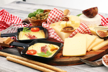 Fototapeta na wymiar Delicious traditional Swiss melted raclette cheese on diced boiled or baked potato and baguette served in individual skillets with salami..