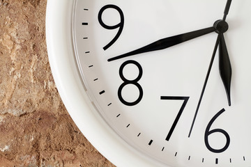 Dinner time concept. A part of white round analog clock face against the background of a red brick wall is showing dinner time.