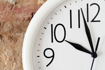 Breakfast time concept. A part of white round analog clock face against the background of a red brick wall is showing breakfast time.