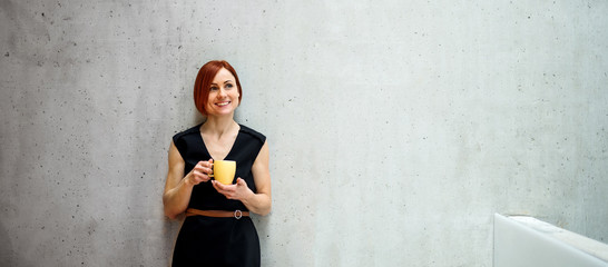 A portrait of young businesswoman standing in office, holding a cup of coffee.