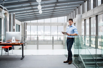 A portrait of young businessman standing indoors in an office.