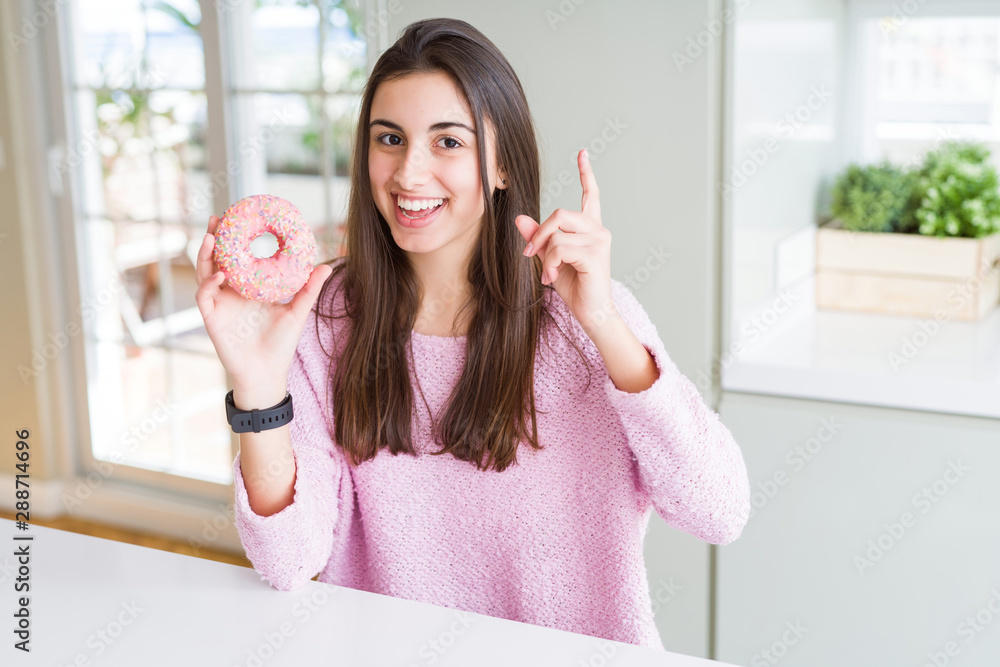 Sticker beautiful young woman eating pink chocolate chips donut surprised with an idea or question pointing 