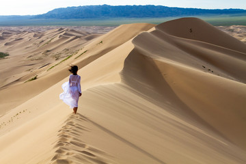 Woman walking in the mongolian desert sand dunes. Young woman walking golden sand on a bright...