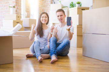 Fototapeta na wymiar Beautiful couple sitting on the floor holding smartphone at new home around cardboard boxes screaming proud and celebrating victory and success very excited, cheering emotion
