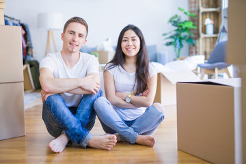 Fototapeta na wymiar Young beautiful couple sitting on the floor at new home around cardboard boxes happy face smiling with crossed arms looking at the camera. Positive person.