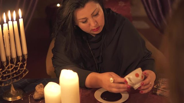 Fortune teller woman in dark room with lots of candles Gives an explaination of future and prediction of fate to a customer with coffee cup thick sediment