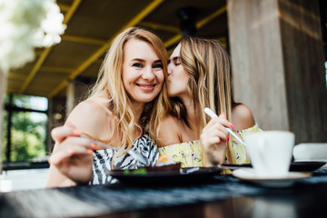 Portrait of two blonde sisters have a breakfast in modern cafe, spend time together. Kisses.