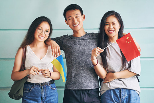 Group of three happy international chinese asian students smiling and holding flags of China and Ukraine in university