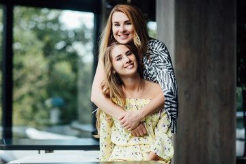 Fototapeta premium Portrait of mother embrathing her pretty daughter and smiling, sitting at summer caffe terrace.