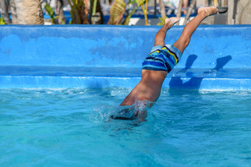 Caucasian boy making jump into swimming pool water. Moment of entrance in water.