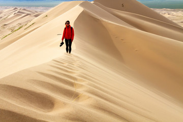 Fototapeta premium Woman walking in the mongolian desert sand dunes. Young woman walking golden sand on a bright summer day, Mongolia holliday vacation concept.