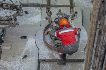 Work driller in red uniform, in helmet and goggles. He with the help of an elevator hangs drill...