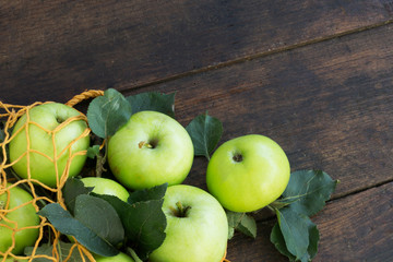 Green apples in a string bag on wooden background close up