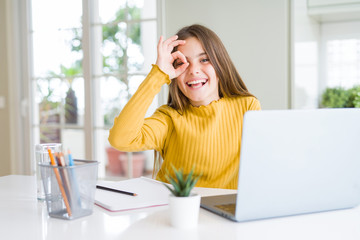 Beautiful young girl studying for school using computer laptop with happy face smiling doing ok sign with hand on eye looking through fingers