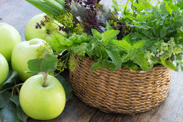 Apples and a basket of fresh  herbs spinach basil parsley mint onion on wooden table