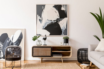 Stylish scandinavian living room interior with gray sofa, black lamp, design commode, tropical plants, sculpture, books and personal accessories. Mock up abstract paintings on the wall. Template.